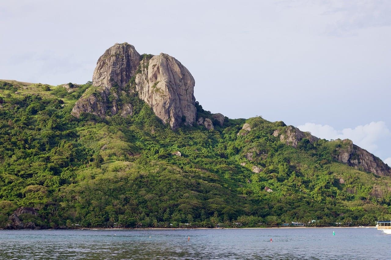 A rocky green peak rising over a calm bay on Kuata Island, Fiji