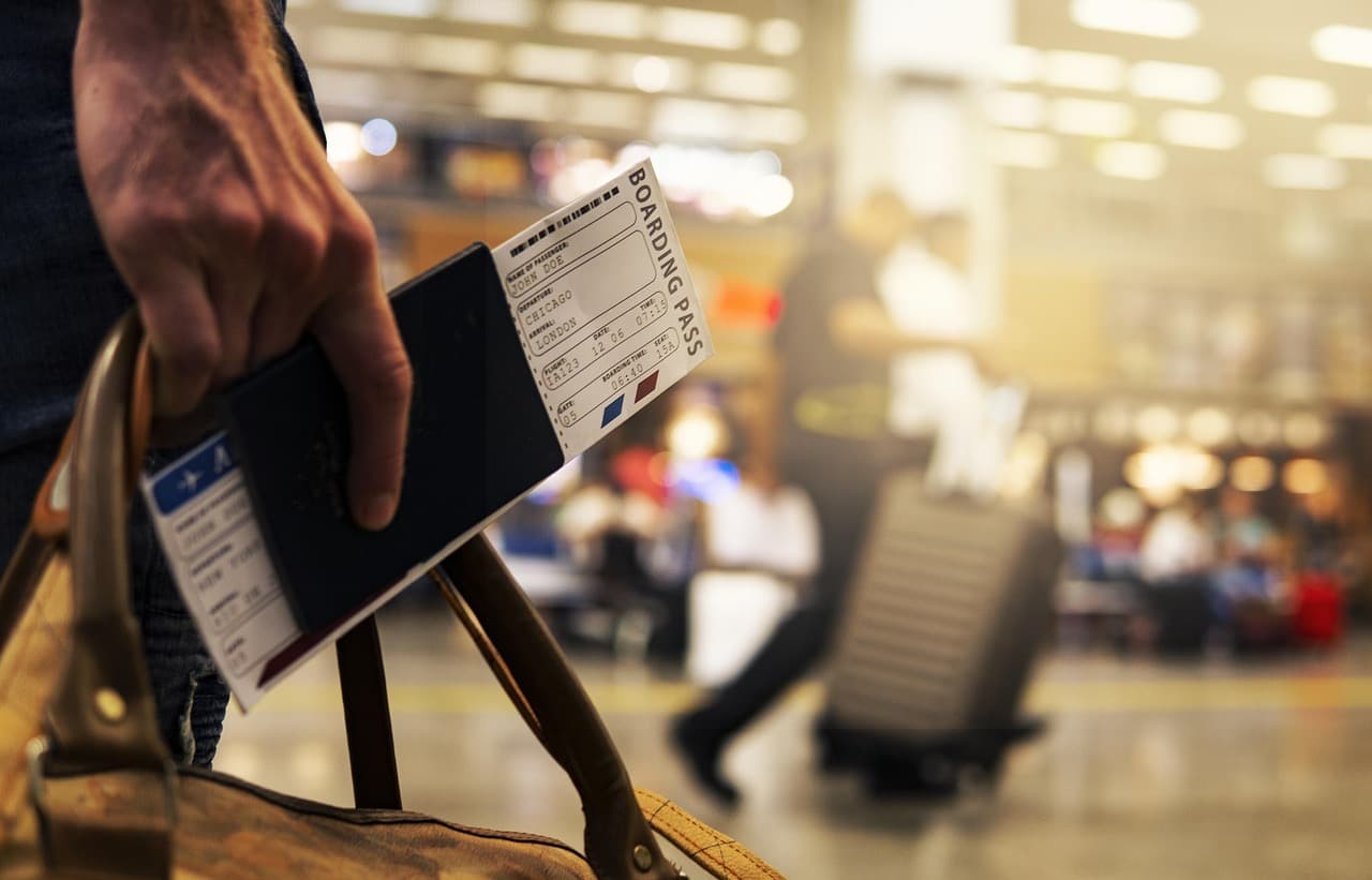 A traveller in an airport holding a passport and a boarding pass