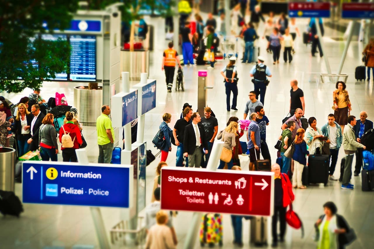 A crowded airport hall with signs for information and police