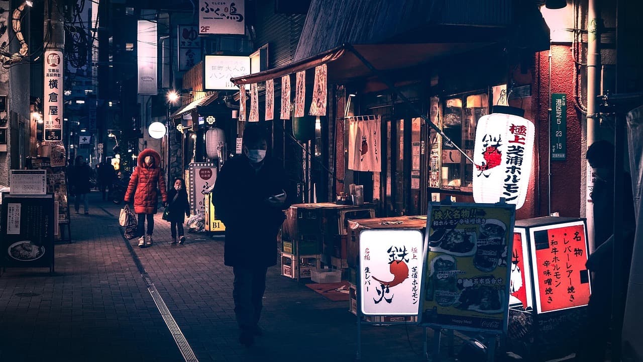 A narrow Tokyo street at night, lit by shop signs