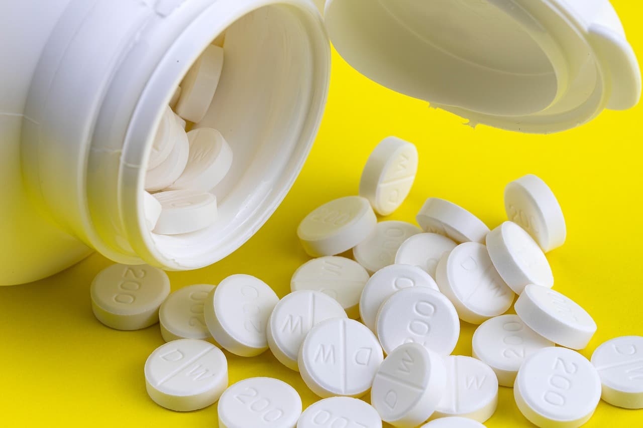 White tablets spilling from an open pill bottle onto a yellow surface