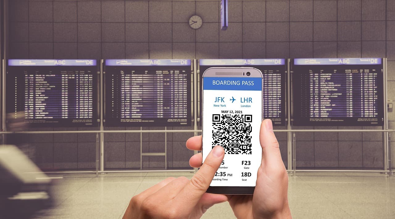 A hand holding a phone showing a boarding pass, in front of airport departure boards