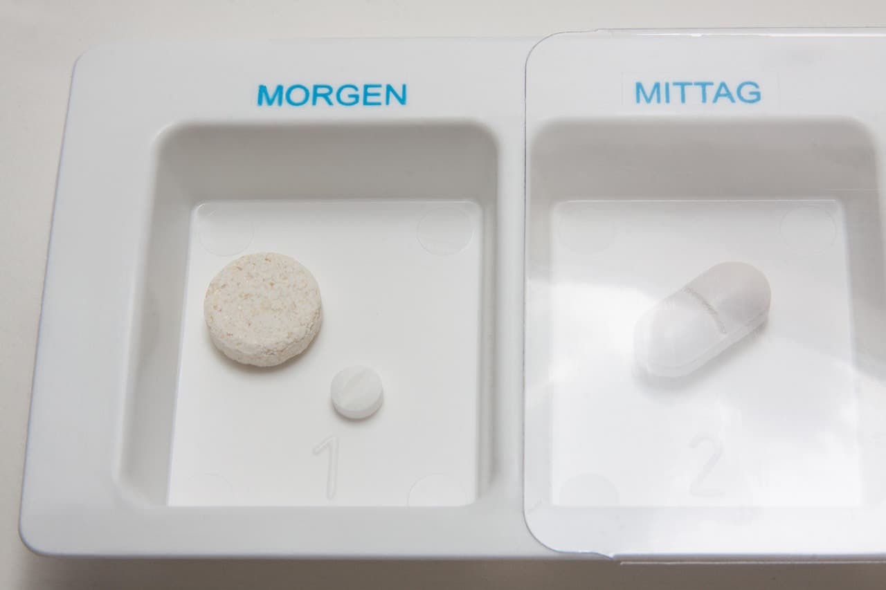 A two-compartment pill organiser labelled morning and midday, holding a tablet and a capsule