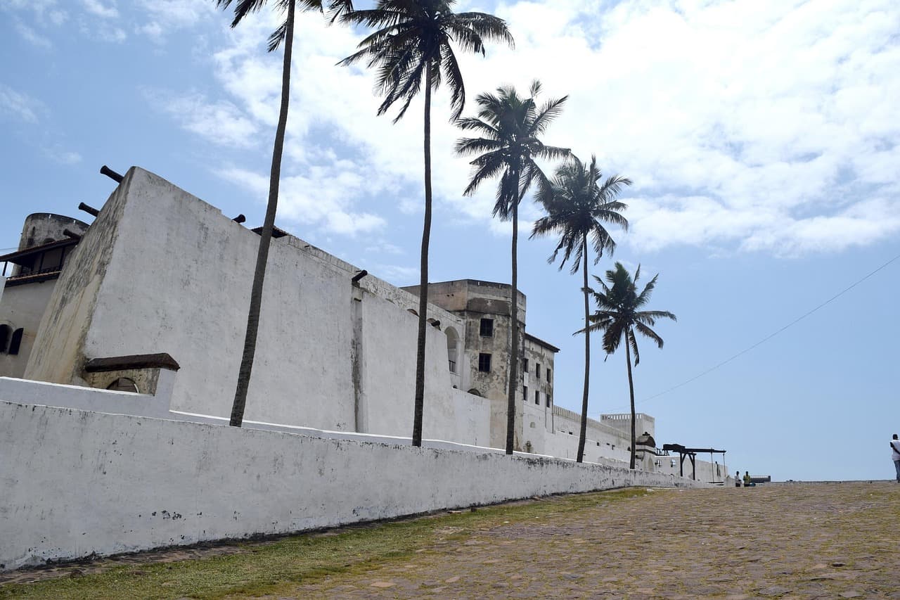 The whitewashed walls of Elmina Castle lined with palm trees, Ghana